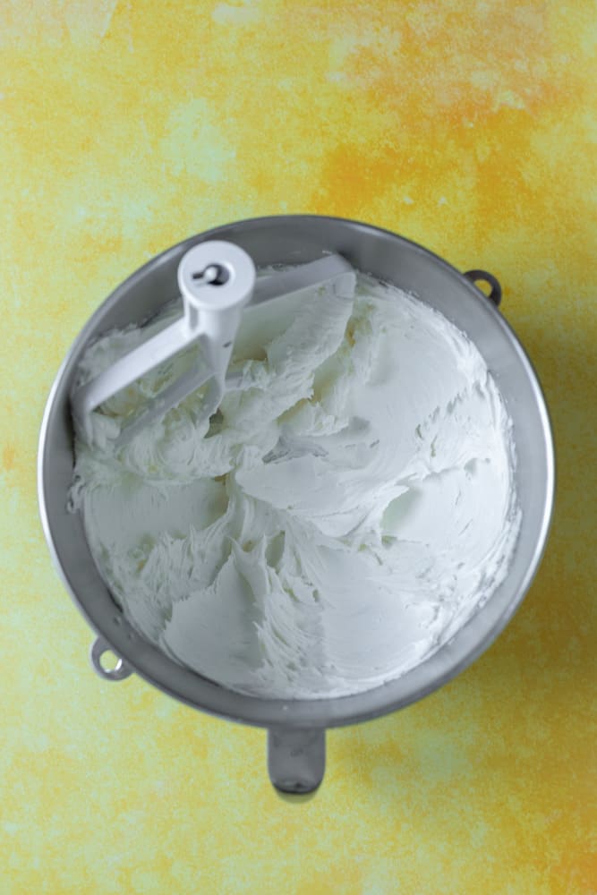 Creamed butter and powdered sugar in a mixer bowl on a yellow surface.