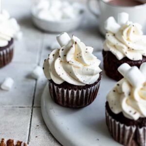 Hot chocolate cupcakes on a white plate with hot cocoa in the background.