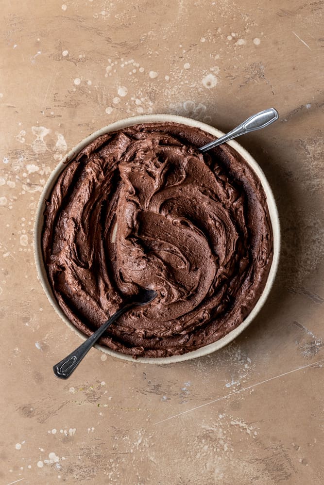 Chocolate buttercream swirled in a bowl with two spoons inside.