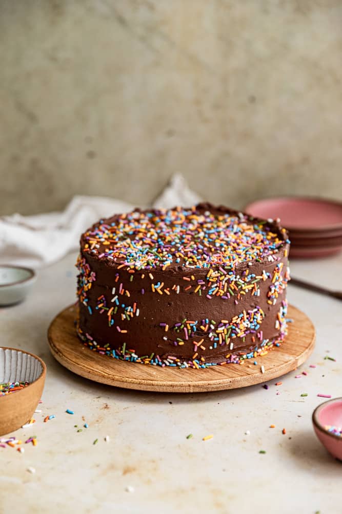 A chocolate cake with sprinkles on a wooden serving piece.