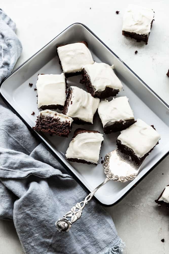 Brownies with cream cheese topping in a white tray on a white surface.