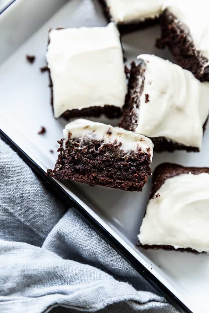A brownie with cream cheese frosting on its side in a white pan.