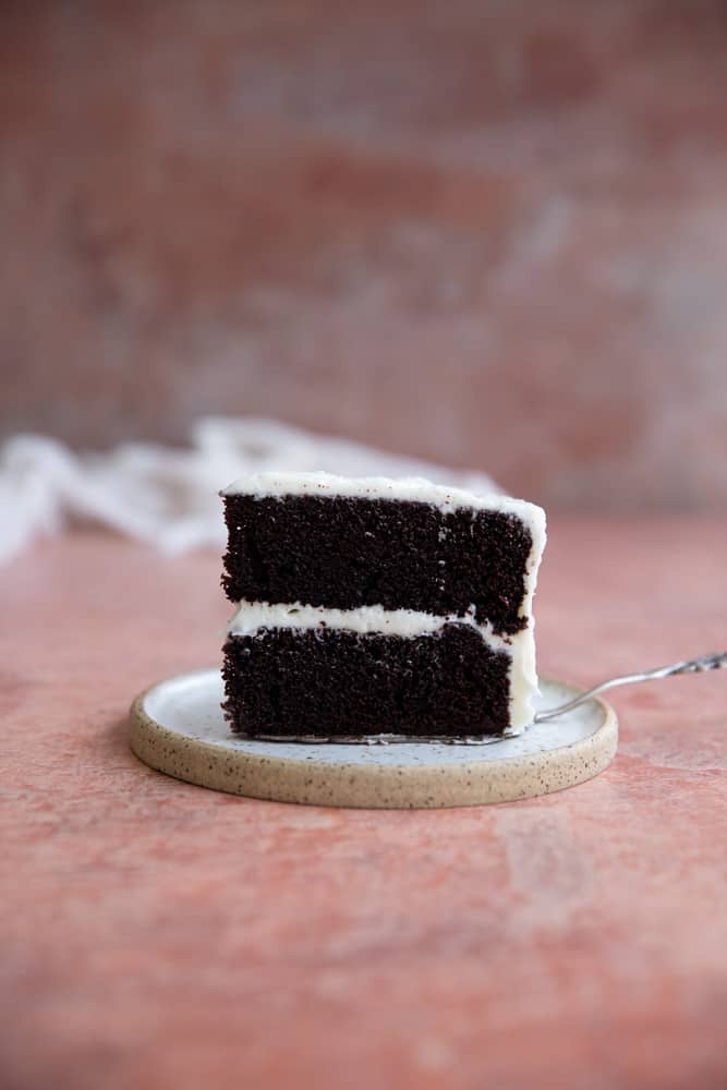 A slice on chocolate cake with cream cheese frosting sitting on a plate.