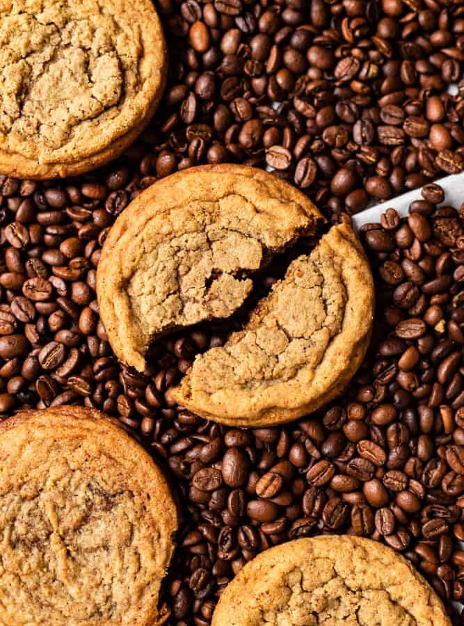 A cookie broken in over lying over coffee beans.