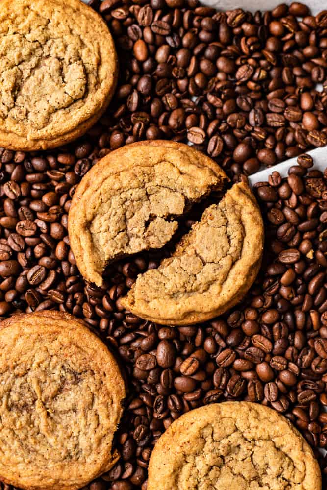 A cookie broken in over lying over coffee beans.