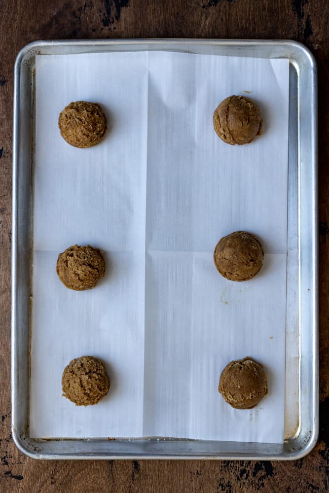 6 coffee cookie dough balls lined up on a parchment lined sheet tray.