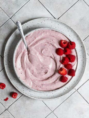 Raspberry cream cheese frosting in a bowl topped with fresh raspberries