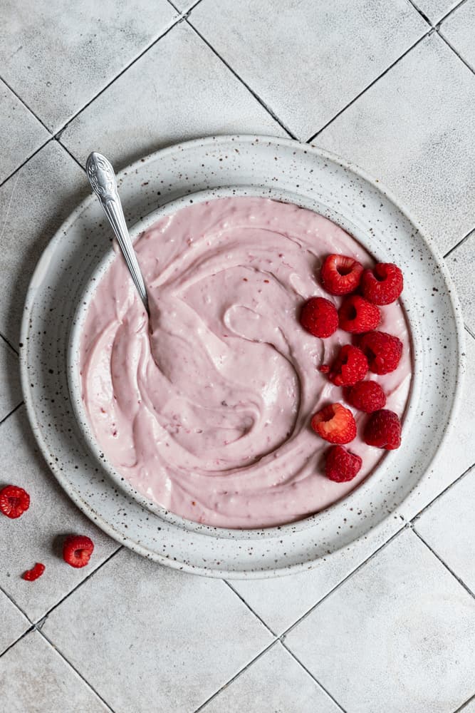 Raspberry cream cheese frosting in a bowl topped with fresh raspberries