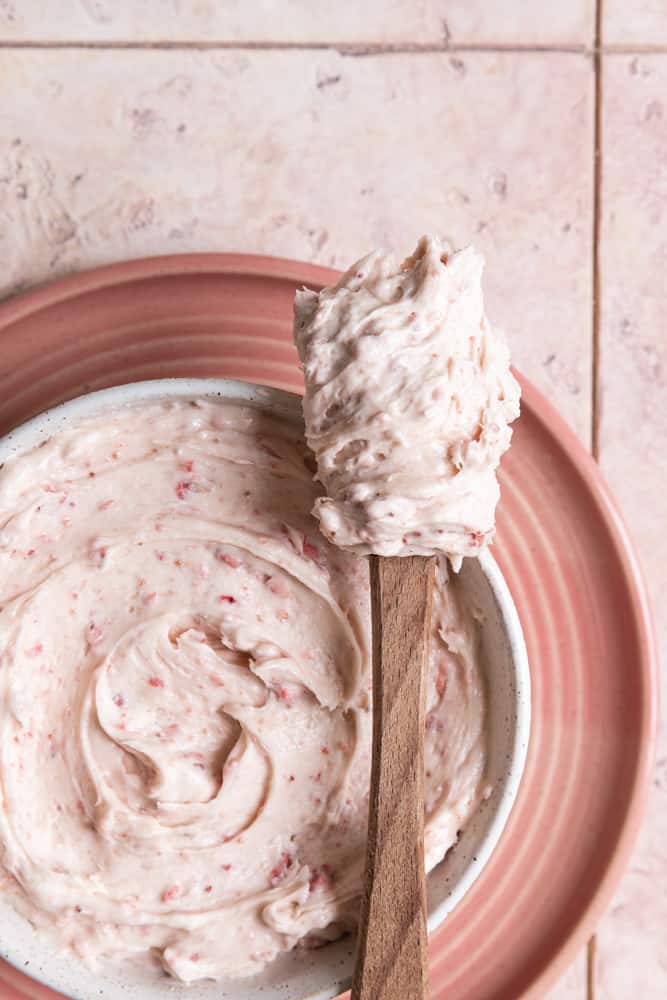 Strawberry cream cheese frosting on a spatula next to a bowl.