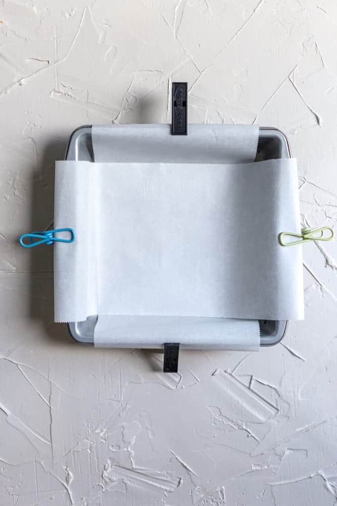 An 8x8 pan lined with parchment paper and clips holding it down.