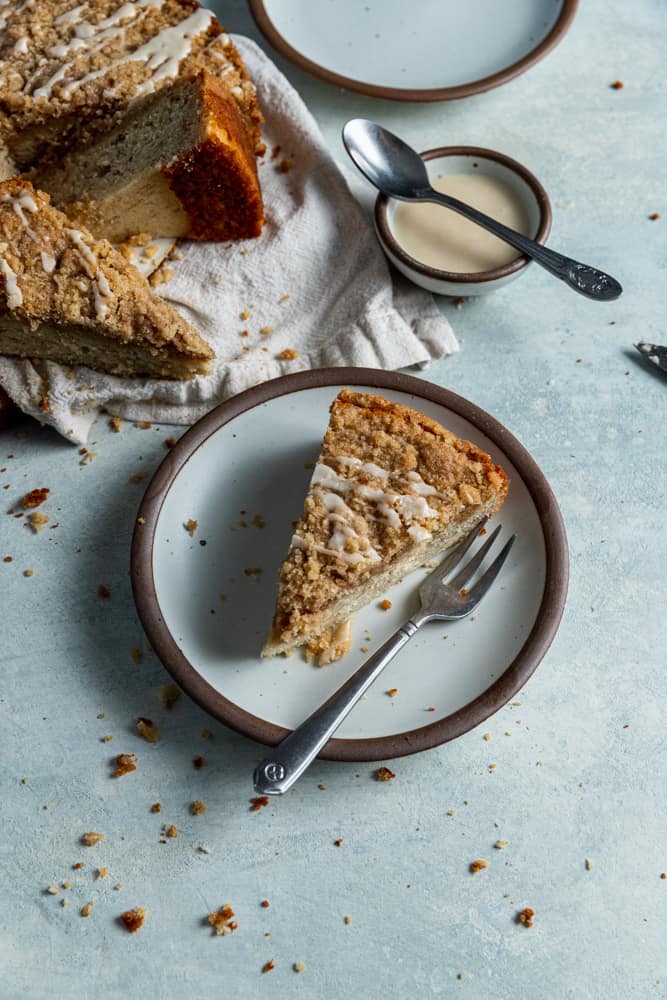 A slice of coffee cake on a plate with a small fork. 