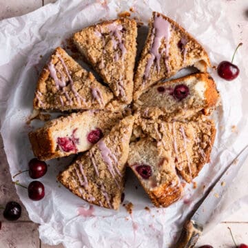 A cherry coffee cake cut into slices on parchment paper.
