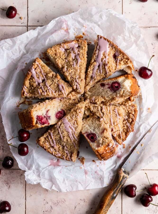 A cherry coffee cake cut into slices on parchment paper.