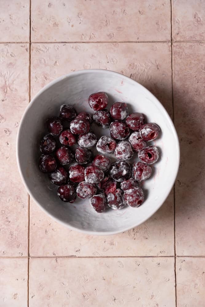 Flour dusted cherries in white bowl.