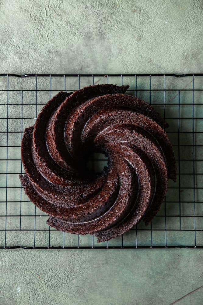 A chocolate bundt cake on a cooling rack on a green surface.