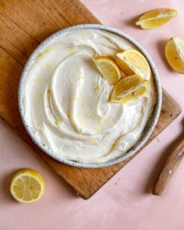 Lemon cream cheese frosting in a bowl with lemon slices on top sitting on a wooden cutting board.