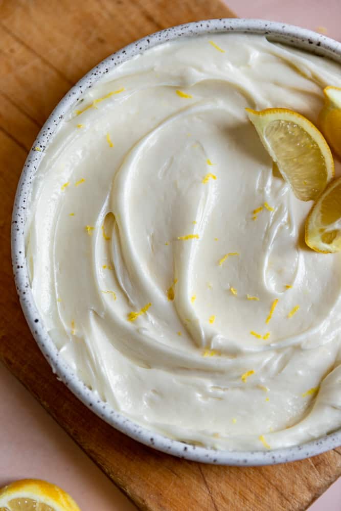 Lemon cream cheese frosting swirled into a bowl with lemon zest on top. 