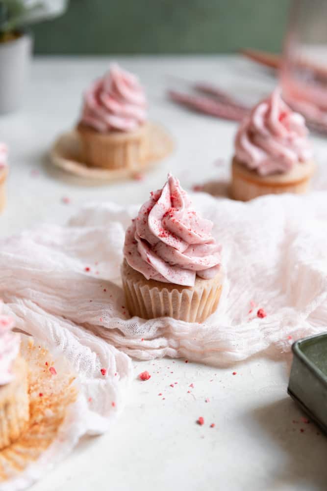 A strawberry cupcake sittong on cheesecloth on a gray surface.