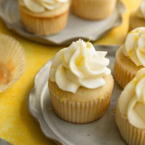 A lemon cupcake with frosting and lemon zest sitting on a gray ruffled plate.