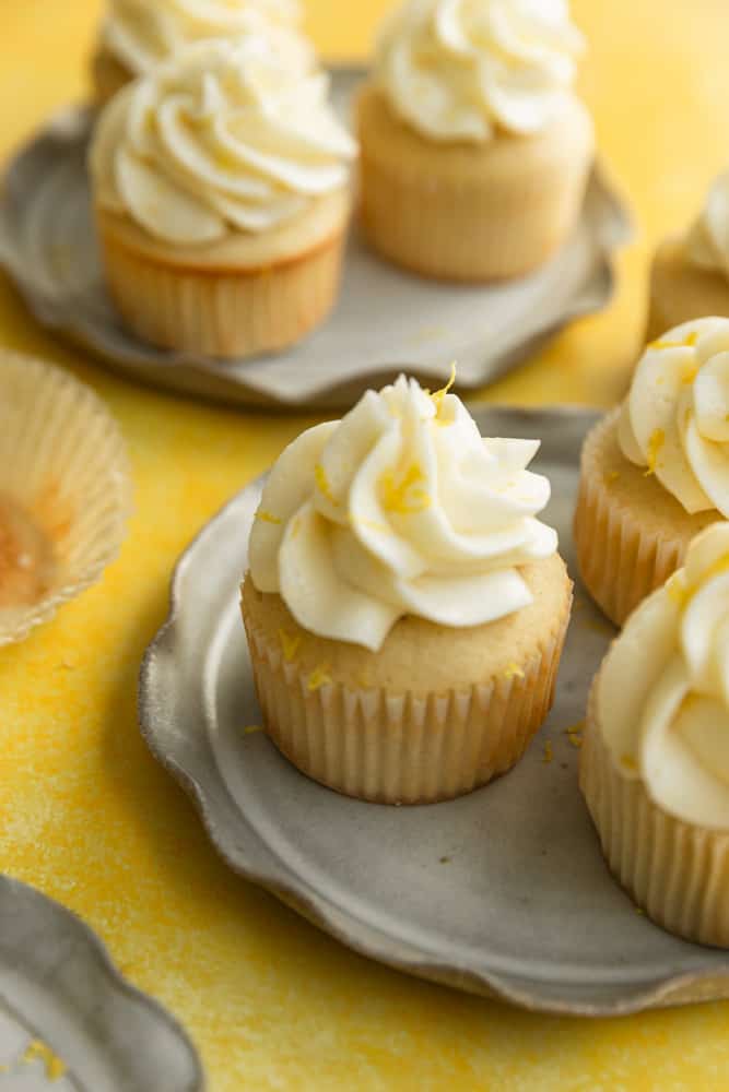 A lemon cupcake with frosting and lemon zest sitting on a gray ruffled plate. 