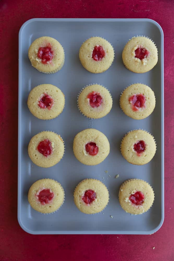 Cupcakes filled with strawberry filling on a sheet tray.