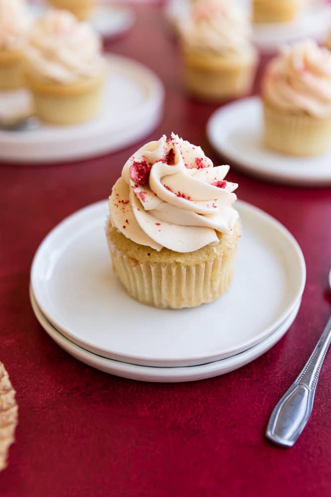 A strawberry filled cupcake with vanilla frosting on 2 small white plates on a red surface.