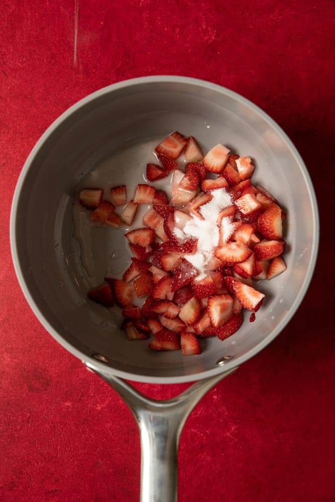 Strawberries and sugar in a small pot.