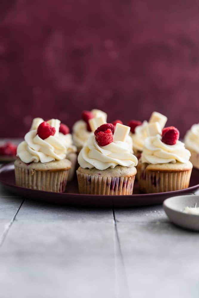 White chocolate raspberry cupcakes on a maroon plate.