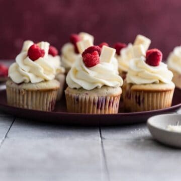 White chocolate raspberry cupcakes on a maroon plate.