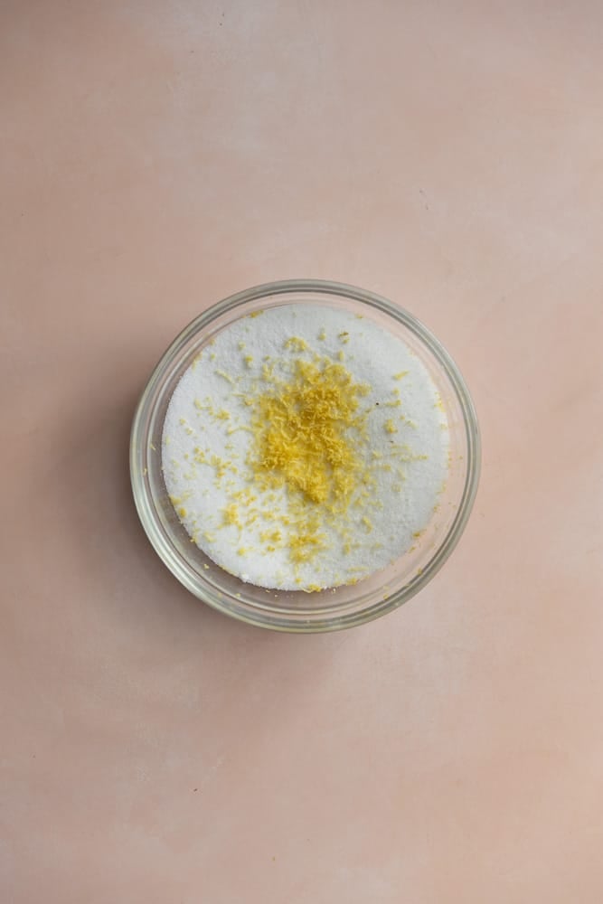 Lemon zest on top of sugar in a glass bowl.