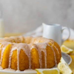 A lemon pudding bundt cake with a white glaze on top on a yellow surface.