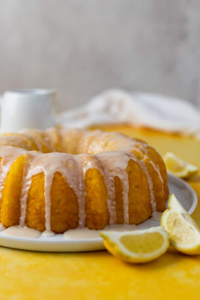 A lemon pudding bundt cake with a white glaze on top on a yellow surface.
