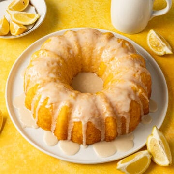 Lemon pudding bundt cake on a white plate on a yellow surface.plate with