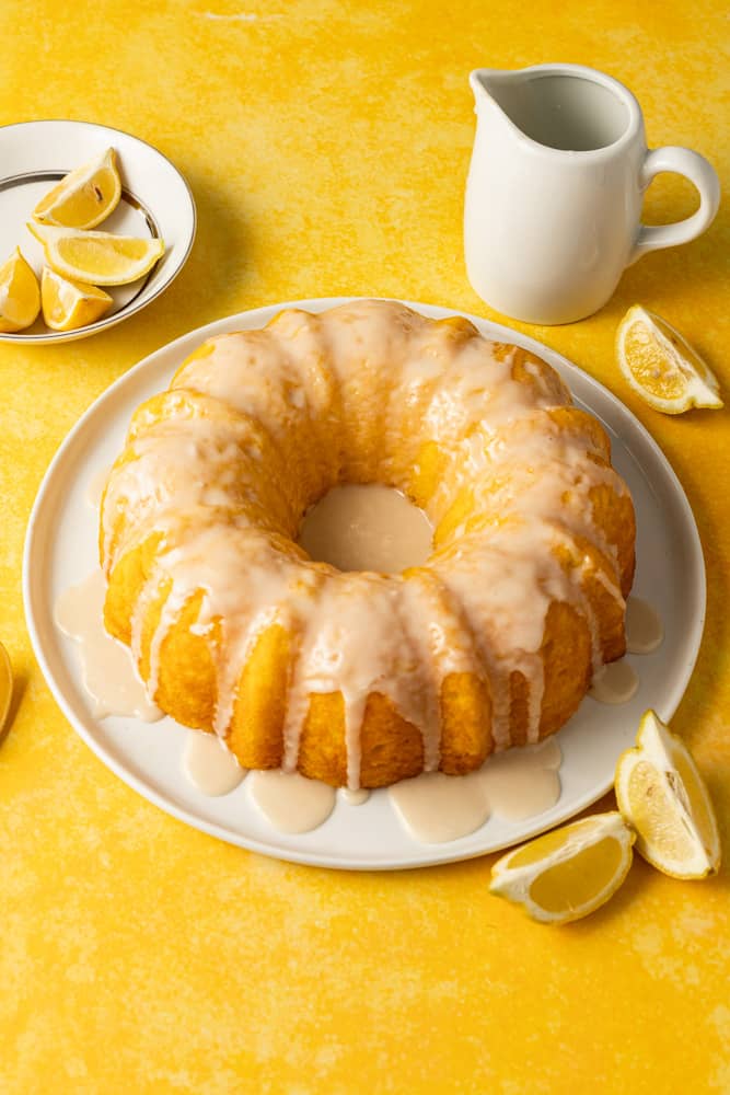 Lemon pudding bundt cake on a white plate on a yellow surface.plate with 