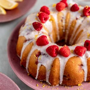 A closeup of a lemon raspberry bundt cake garnished with white glaze, raspberries, and lemon zest.