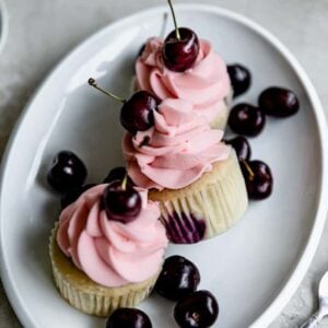 3 cherry cupcakes on an oval platter with fresh cherries around.