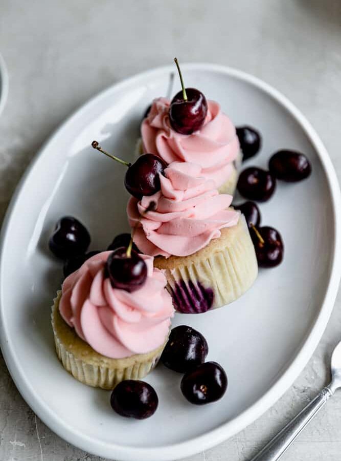 3 cherry cupcakes on an oval platter with fresh cherries around.