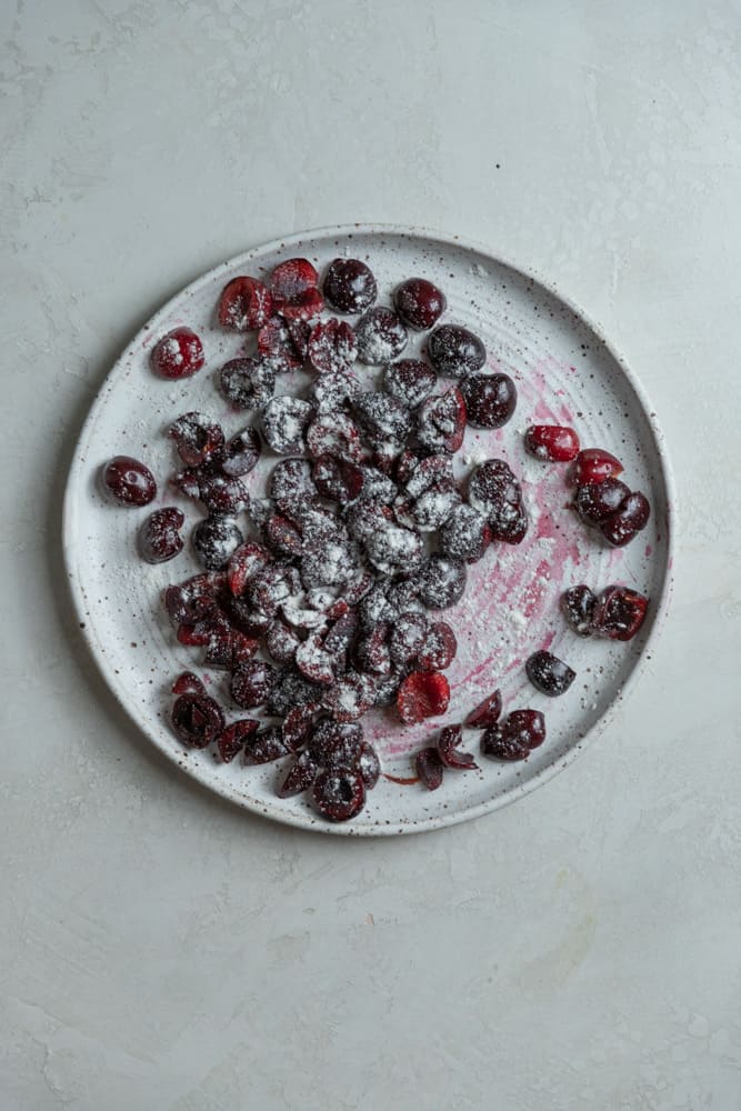 Pitted cherries tossed in flour on a white plate.