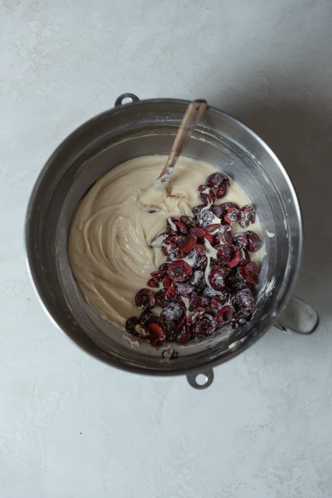 Cherries tossed into cupcake batter in a mixing bowl.