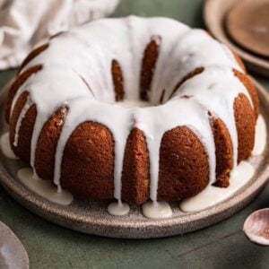 A gingerbread bundt cake topped with a white glaze on a brown plate.