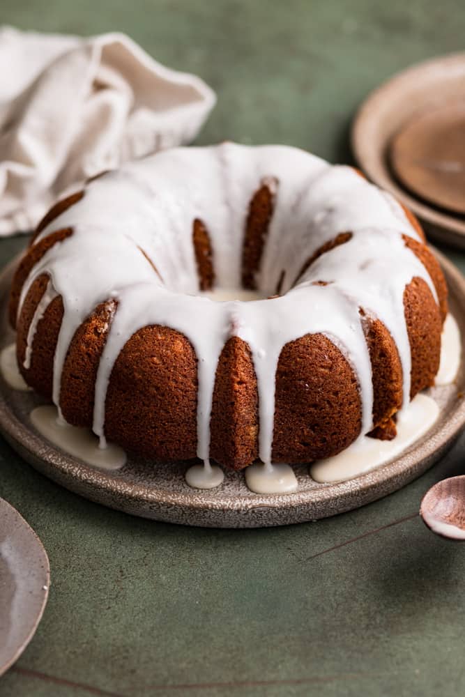 A gingerbread bundt cake topped with a white glaze on a brown plate.