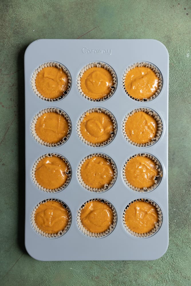 A muffin tin with orange cupcake batter inside.