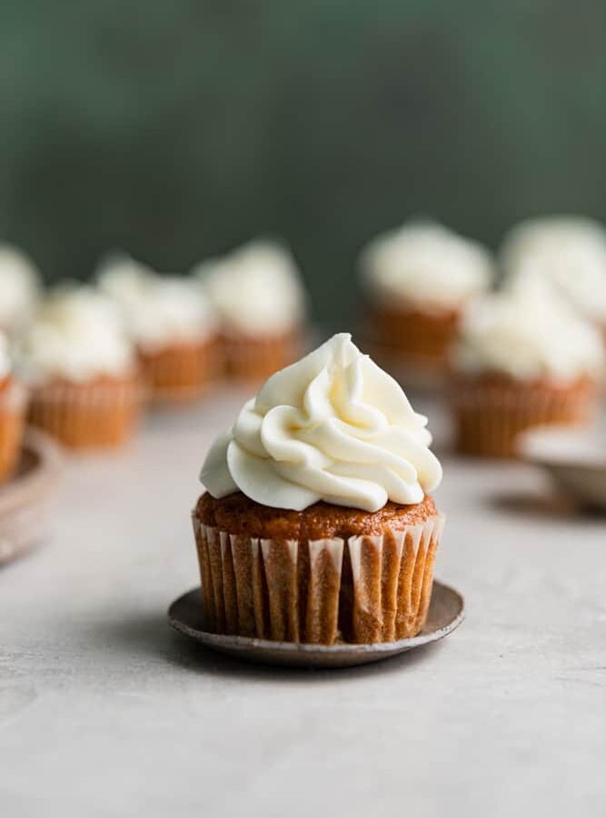 A pumpkin cupcake with cream cheese frosting on a small plate.
