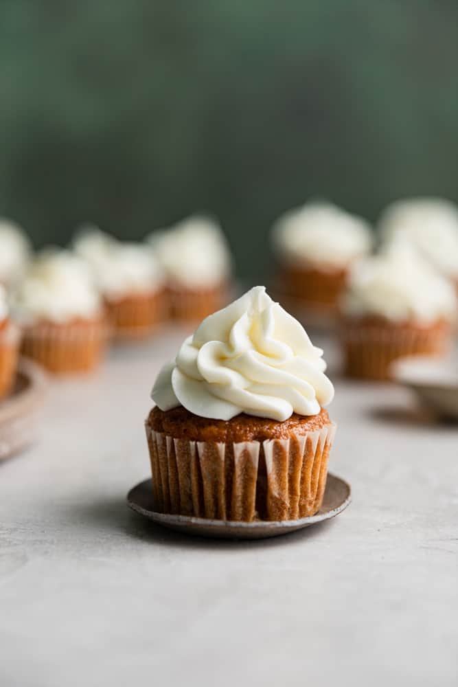 A pumpkin cupcake with cream cheese frosting on a small plate.