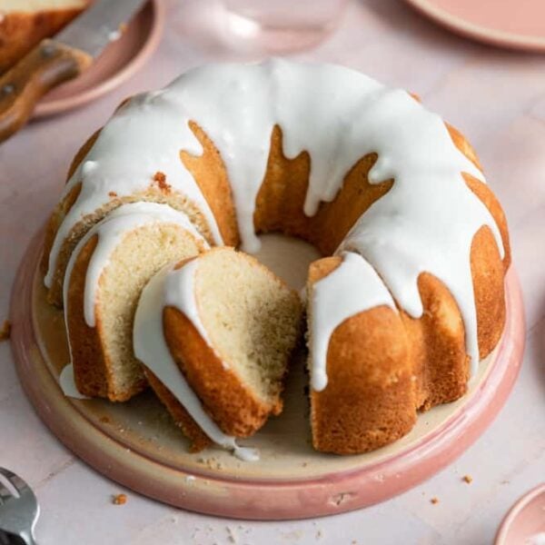 A vanilla bundt cake with slices cut out of it on a pink plate.