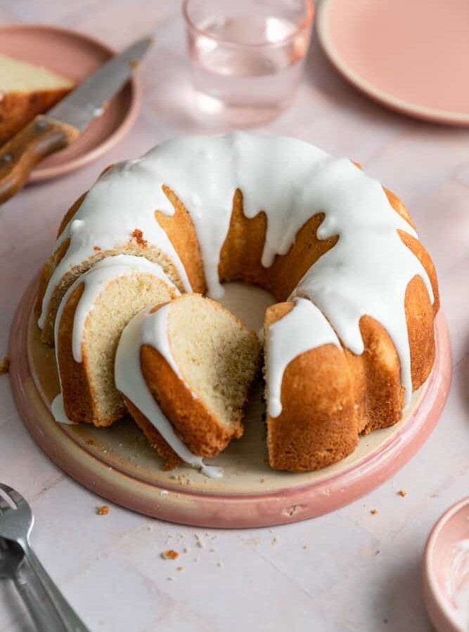 A vanilla bundt cake with slices cut out of it on a pink plate.