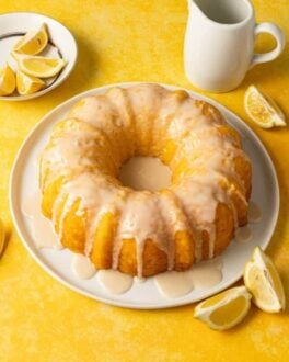 Lemon pudding bundt cake on a white plate on a yellow surface.plate with