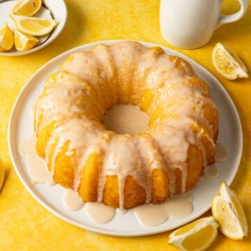 Lemon pudding bundt cake on a white plate on a yellow surface.plate with