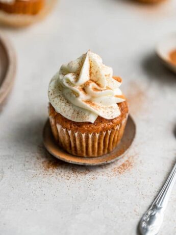 A pumpkin cupcake with white frosting dusted with cinnamon on a small plate.