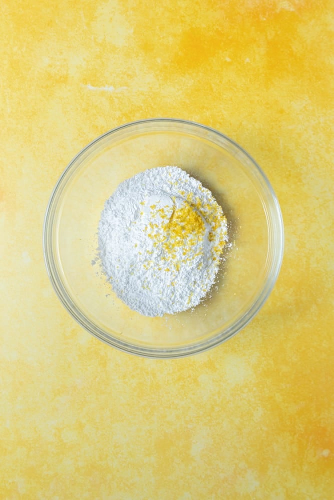Powdered sugar in a bowl with lemon zest on top.